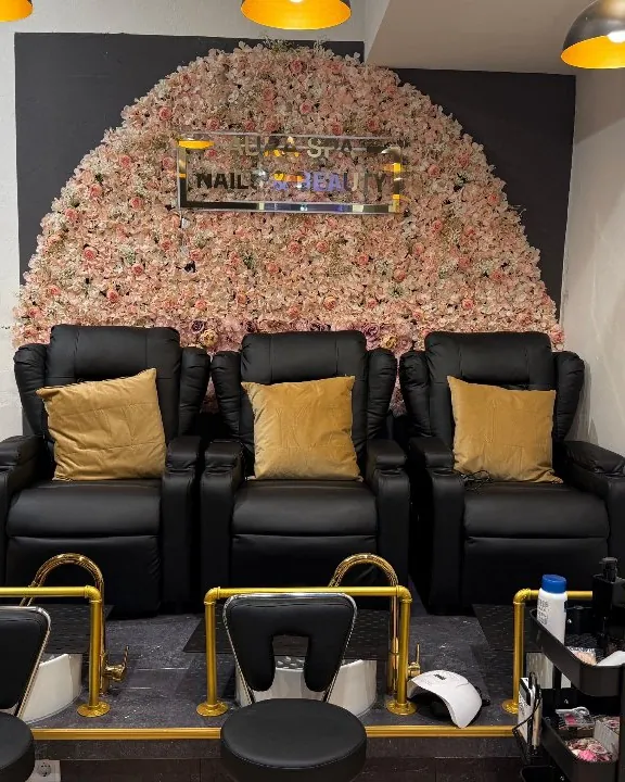 Pediküre-Lounge mit schwarzen Sesseln, goldenen Kissen und Blumenwand